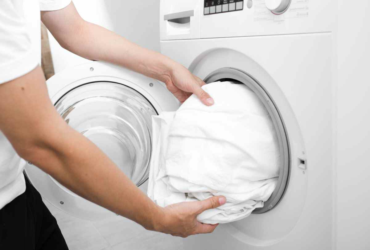 männliche Hand, die ein Tuch in die Waschmaschine legt.  Bettwäsche aus Leinen waschen