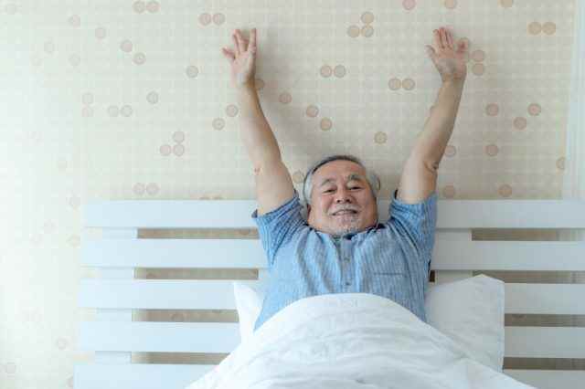 glücklicher älterer Mann, gute Gesundheit, wacht morgens mit Freude in seinem Schlafzimmer auf