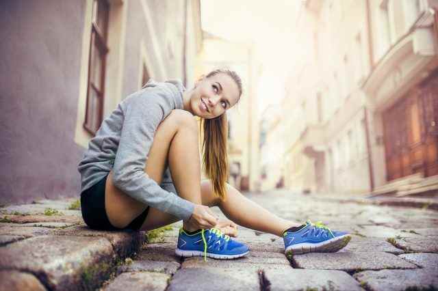 Junge Läuferin bindet ihre Laufschuhe auf gefliestem Bürgersteig in der Altstadt
