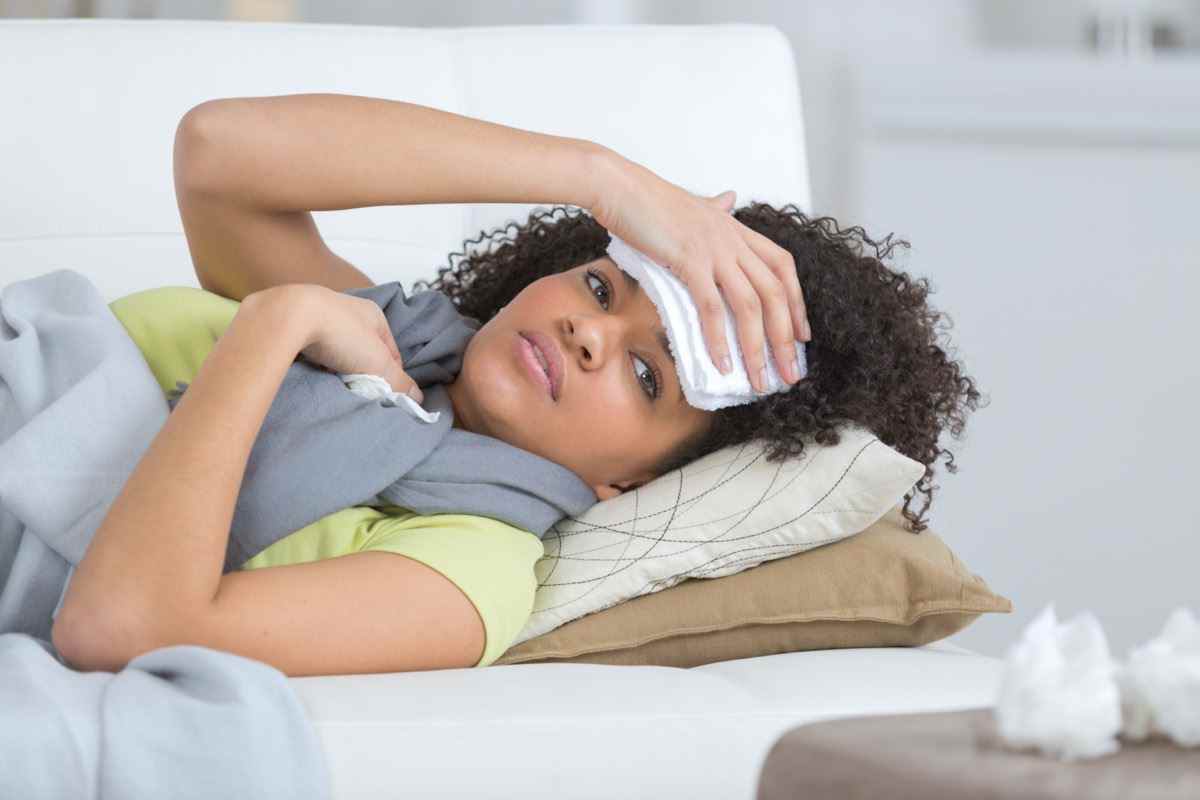 junge Frau sitzt auf einer Couch und hat starke Kopfschmerzen