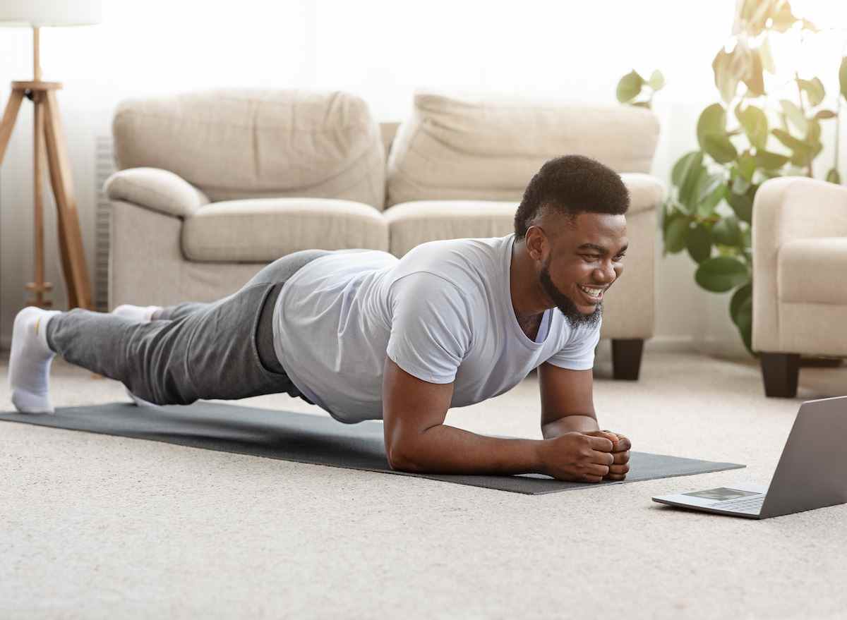 Mann zu Hause macht modifizierte Planke auf Yogamatte im Wohnzimmer