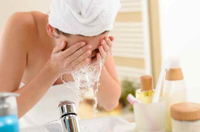 Frau spritzt Gesicht mit Wasser über dem Waschbecken im Badezimmer