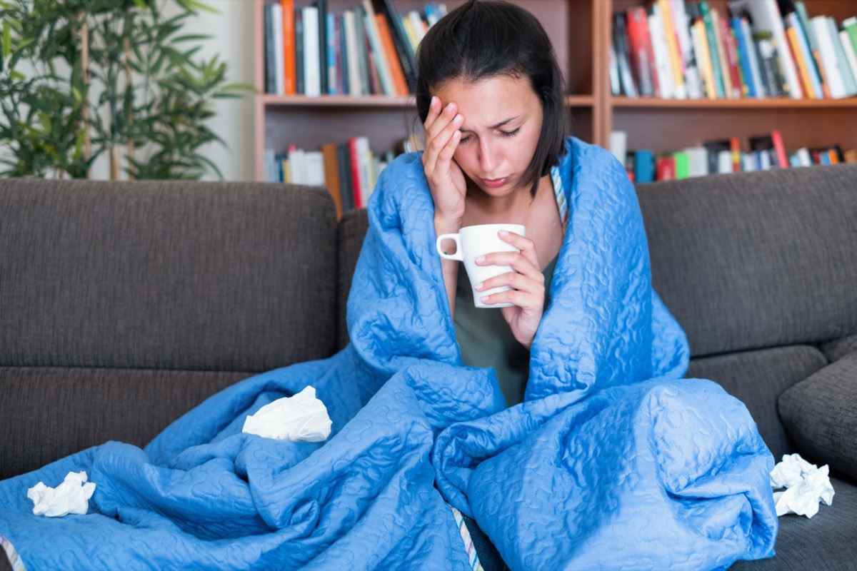 Frau mit einer Decke auf dem Sofa mit hohem Fieber und Grippe
