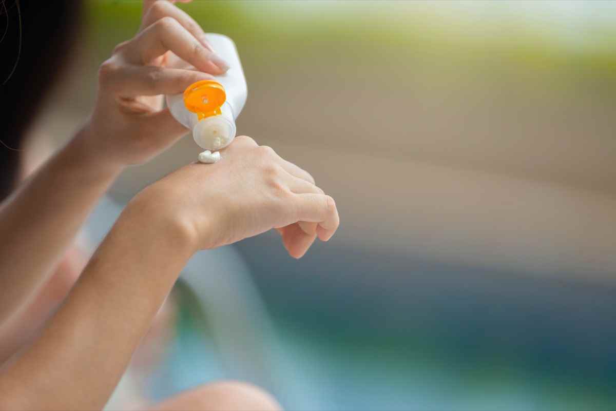 Frauenhände gießen Sonnencreme zur Hand und halten eine leere Sonnencreme UV-Schutzlotion-Flasche, die eine Kosmetikvorlage für Ihr Design verpackt und Platz zum Hinzufügen Ihres Inhalts lässt