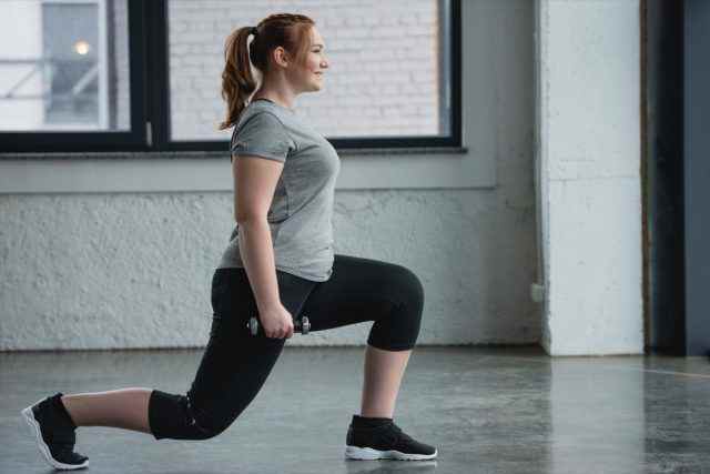 Plus-Size-Frau, die Ausfallschritte mit Hantel im Fitnessstudio durchführt