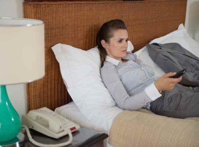Müde Geschäftsfrau vor dem Fernseher im Hotelzimmer