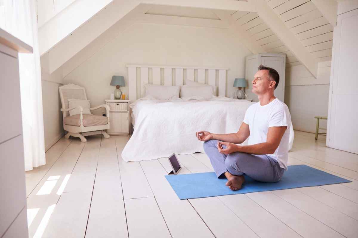 Reifer Mann mit digitalem Tablet mit Meditations-App im Schlafzimmer