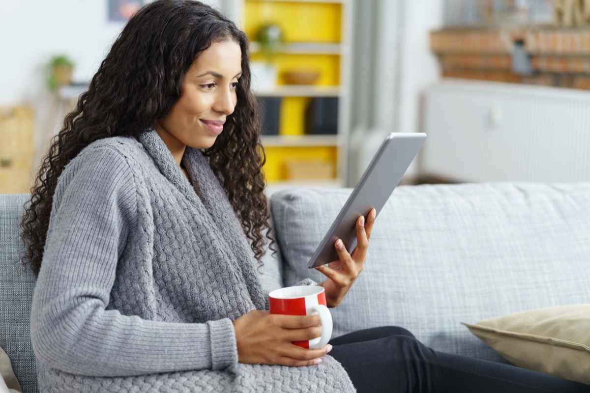 Frau liest zu Hause auf Tablet mit einer Tasse Kaffee in der Hand