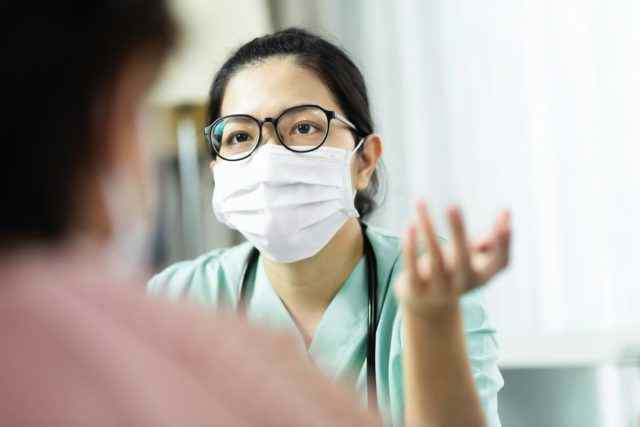 Ärztin in grüner Uniform trägt eine Brille und eine chirurgische Maske, die ältere Patientinnen im Krankenhaus berät, berät und berät