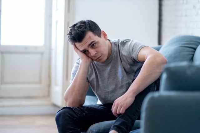 Porträt eines jungen Mannes, der depressiv und verzweifelt weinend allein im Sofahaus weinte und unter emotionalen Schmerzen und Unglück leidet