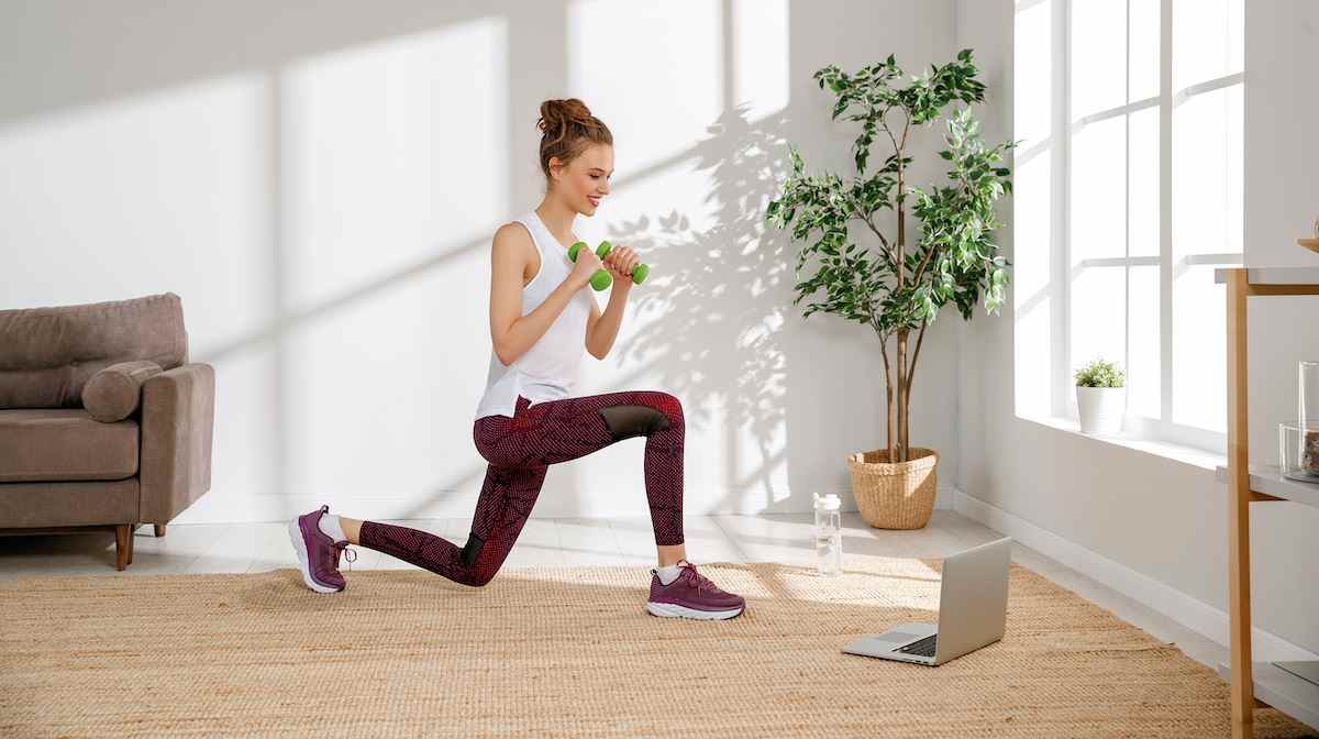 Seitenansicht einer aktiven jungen Frau in Sportbekleidung, die Übungen mit Hanteln macht und während des Fitnesstrainings zu Hause Videos auf dem Laptop ansieht