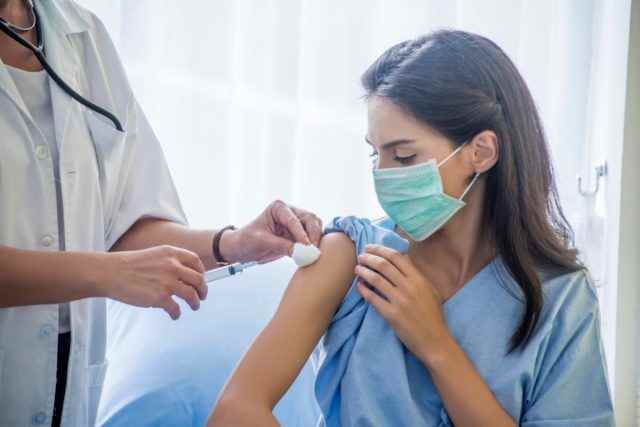 Die Spritzenspritze der Ärztin an die junge Patientin setzte im Krankenhaus eine Maske auf