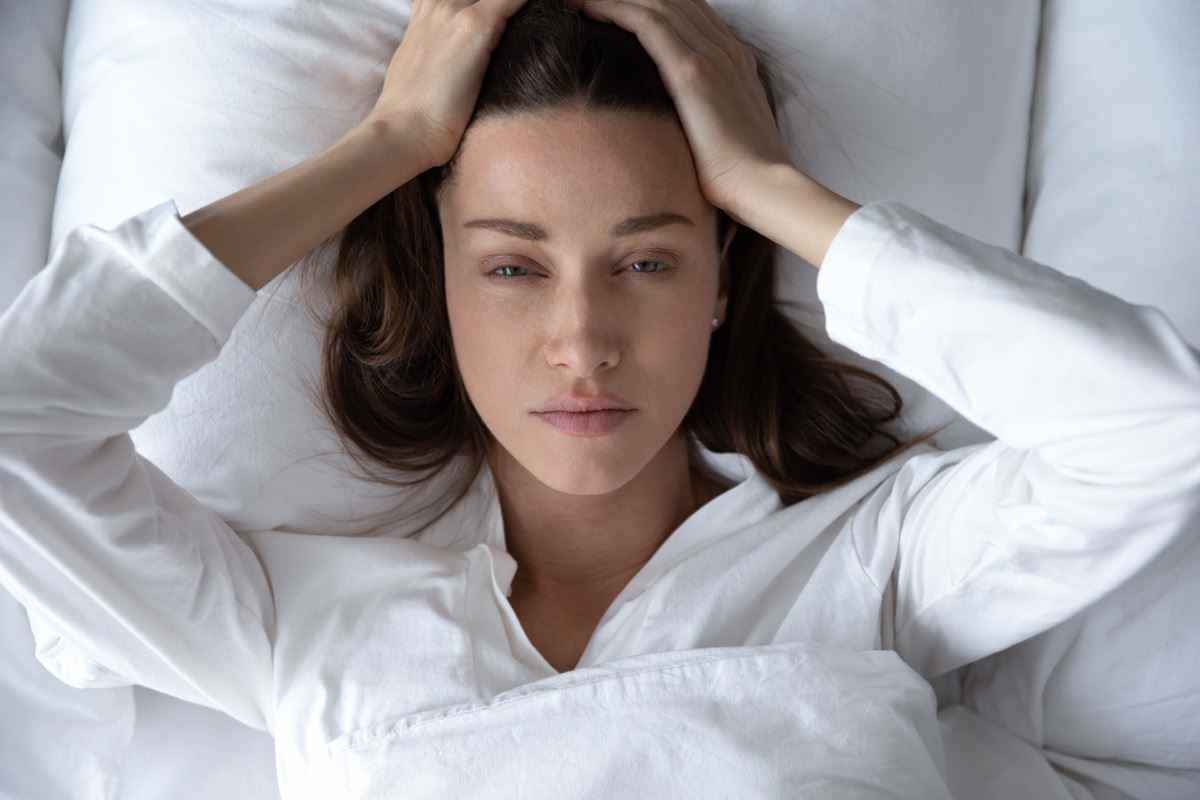 Gestörte Frau, die wach im Bett liegt, leidet an Schlaflosigkeit Kopfschmerzen