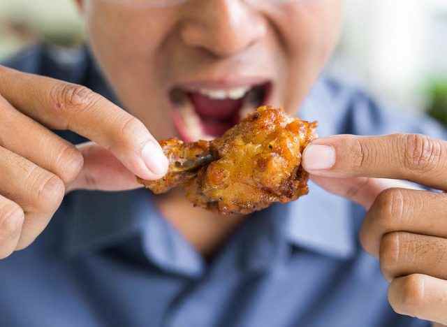 Mann isst einen gebratenen Hühnerflügel