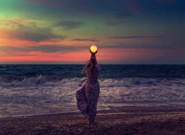 Frau hält Mond am Strand hoch