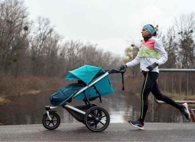 Frau in Trainingskleidung joggt im Winter mit Kinderwagen