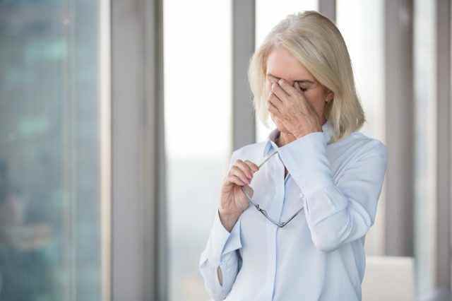 Müde reife Frau nimmt Brille ab, die unter Kopfschmerzen leidet