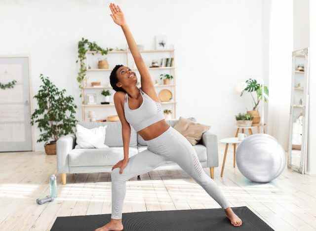 glückliche Frau, die Yoga-Pose im hellen Wohnzimmer macht