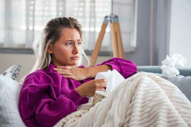 Frau mit ersten Covid-19-Symptomen, Halsschmerzen, Atembeschwerden auf dem Sofa