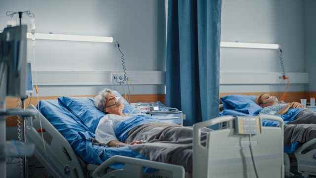 Ältere Frau mit Sauerstoffmaske, die im Krankenhausbett schläft.