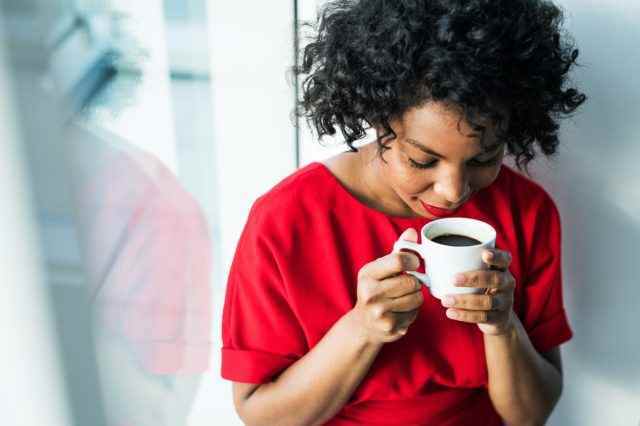 Eine Nahaufnahme einer Frau, die am Fenster steht und eine Tasse Kaffee hält.