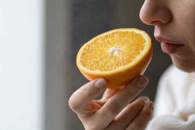Kranke Frau, die versucht, den Geruch von halb frischer Orange zu spüren, hat Symptome von Covid-19, Corona-Virusinfektion - Geruchs- und Geschmacksverlust