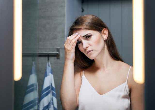 Frau mit Kopfschmerzen vor einem Badezimmerspiegel