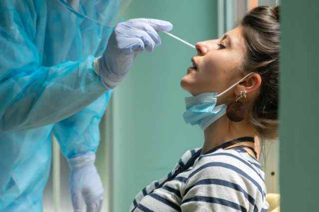 Mitarbeiter des Gesundheitswesens mit Schutzausrüstung führen bei einer Frau einen Coronavirus-Abstrich durch.