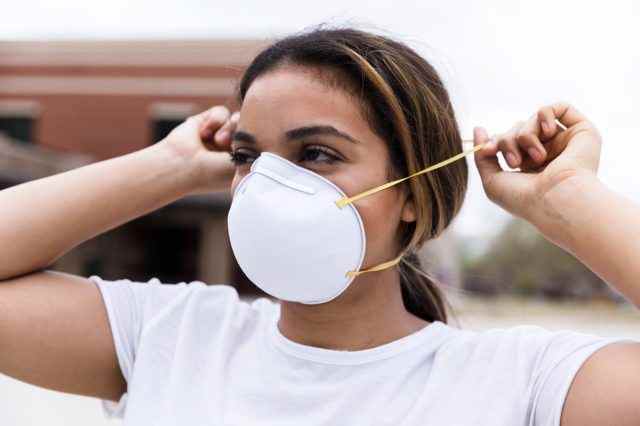 Eine Frau mittleren Alters schützt sich, indem sie eine N95-Gesichtsmaske über Nase und Mund legt.
