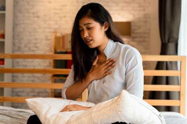 Asiatische Frau, die nachts im Schlafzimmer Schwierigkeiten beim Atmen hat