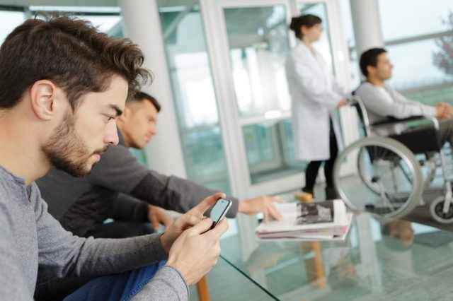 Mann benutzt Smartphone, während er in einer Klinik wartet