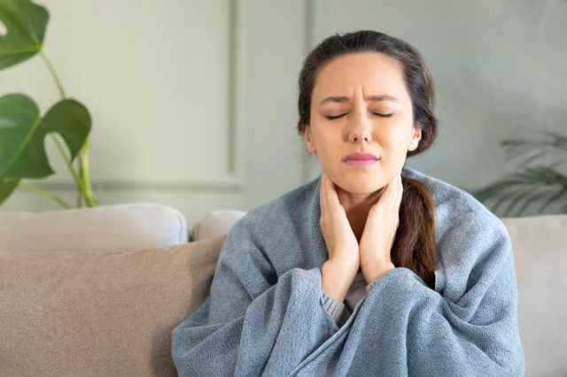 Junge Frau berührt schmerzhaften Hals, Halsschmerzen bei Grippe, Erkältung und Infektion.