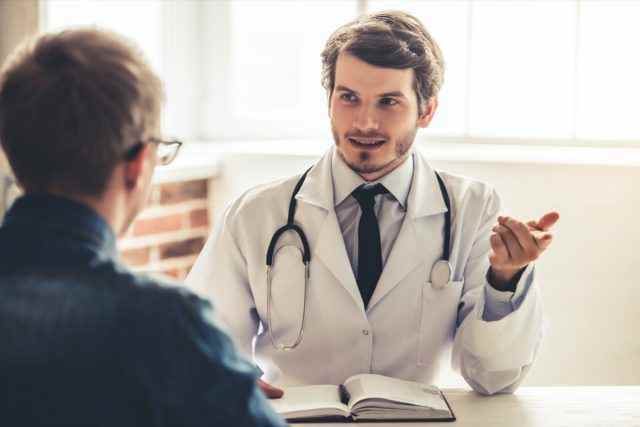 Ein hübscher junger Arzt im weißen Kittel spricht mit seinem Patienten, während er im Büro arbeitet