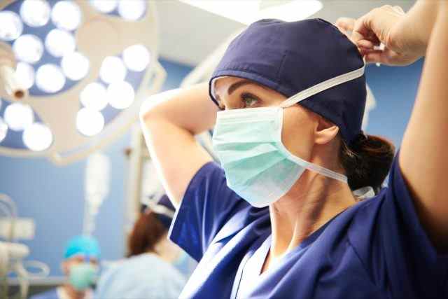 Seitenansicht einer jungen Chirurgin, die ihre OP-Maske bindet