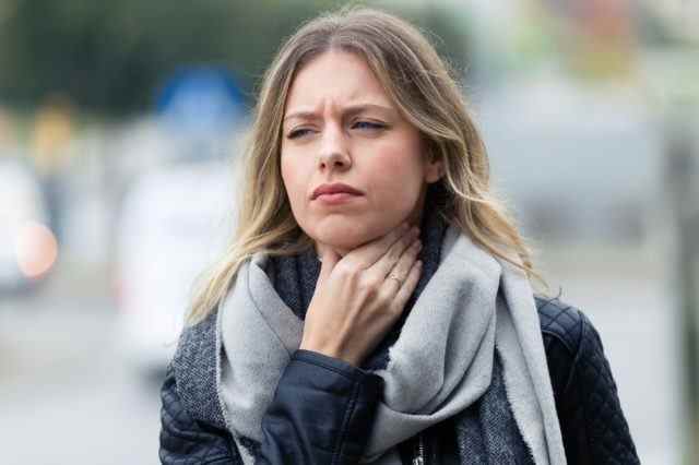 Junge Frau mit Halsschmerzen, die auf die Straße geht.
