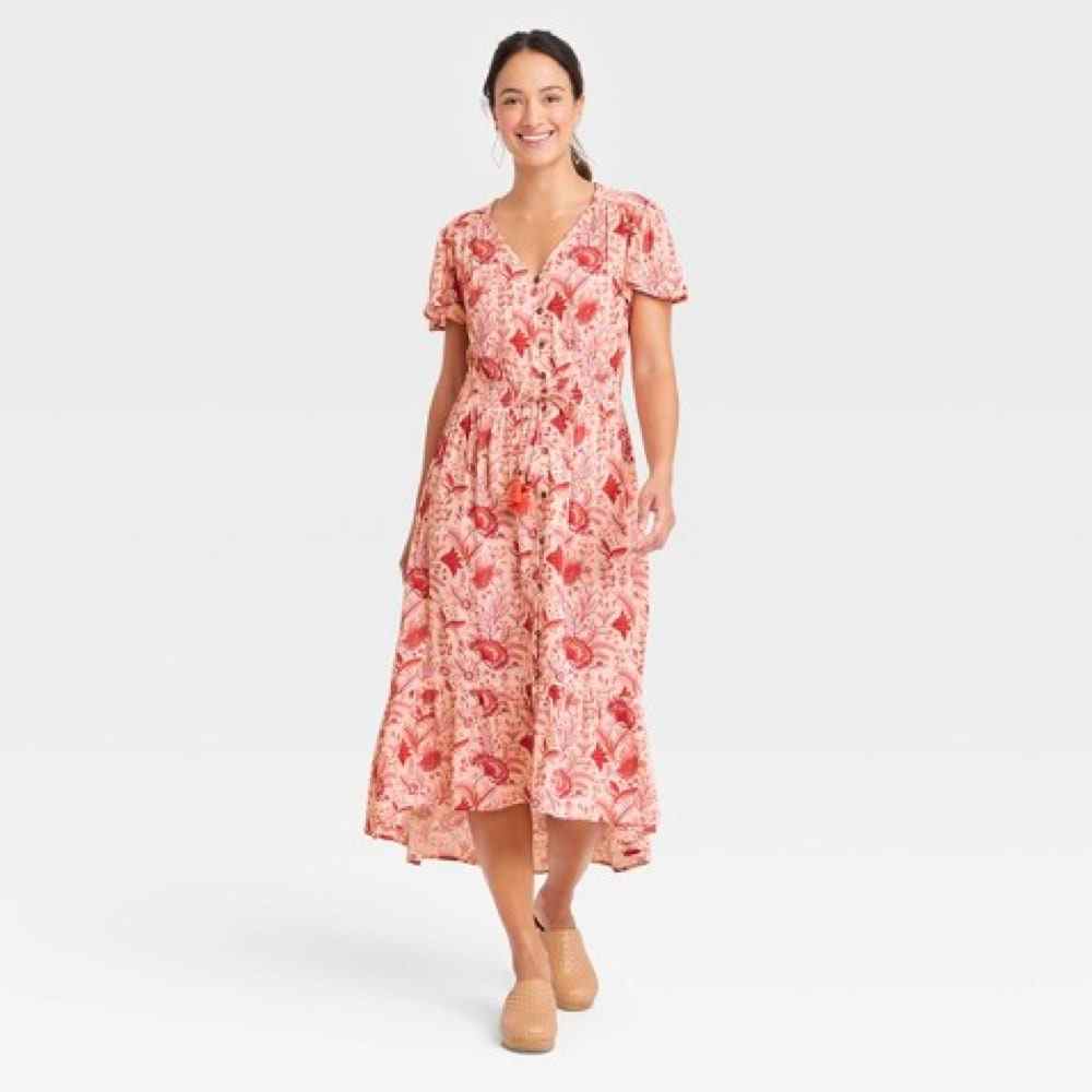Das Model trägt ein knox Rose Flutter Kurzarm-Kleid mit gesmoktem Detail in rosa/rotem Blumendruck