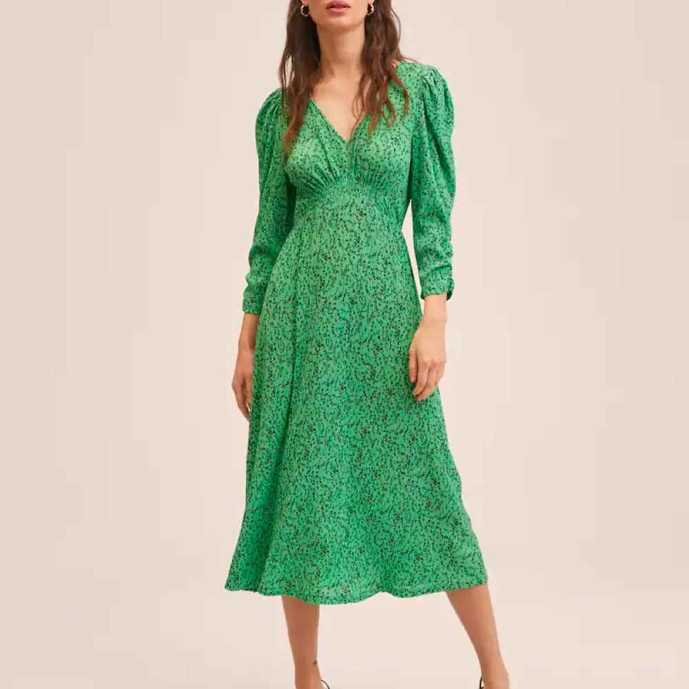 Das Model trägt ein langärmliges, grünes, plissiertes Kleid mit Mango-Print