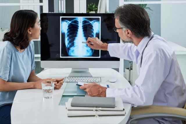 Arzt erklärt dem Patienten die Lungenröntgenaufnahme auf dem Computerbildschirm