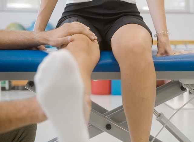 Physiotherapeut hilft dem Patienten bei der Kniestreckung auf dem Tisch, um schwache Knie zu stärken