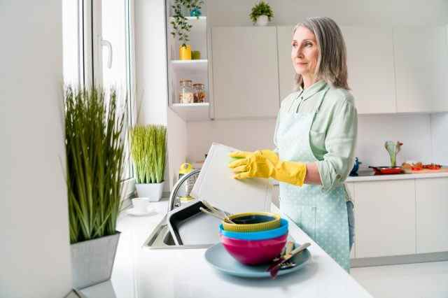 Grauhaarige Frau beim Geschirrspülen.