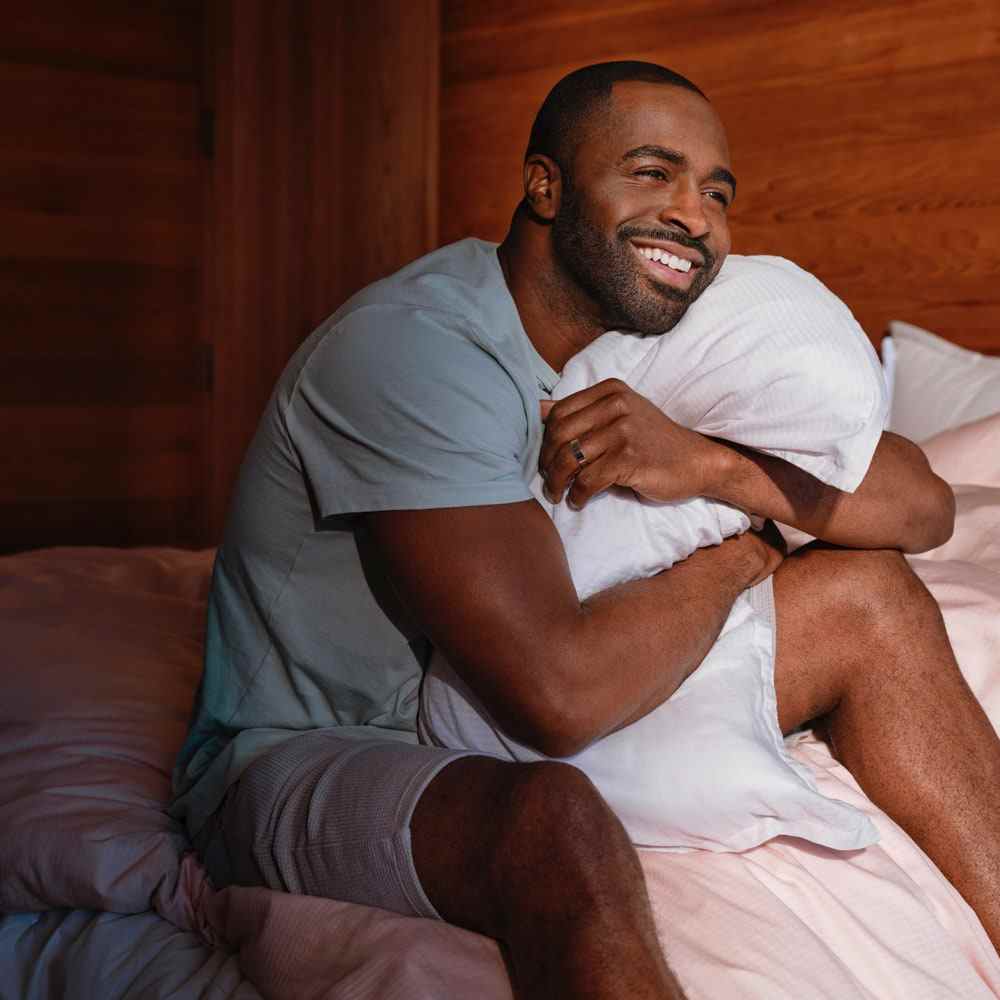 Modell umarmt ein einzelnes Standard-Casper-Schlaf-Low-Loft-Originalkissen auf Bett mit rosa Laken