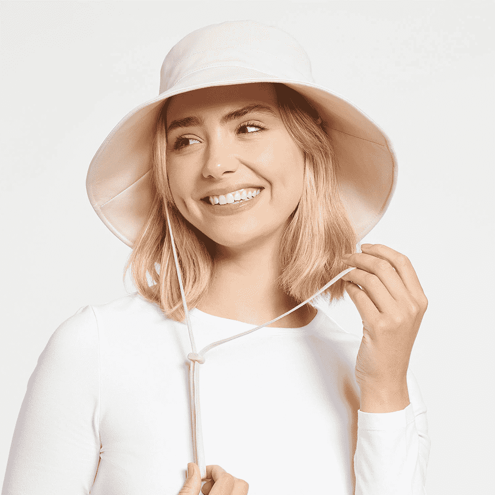 Model lächelt und trägt einen beigen Wende-Strandhut mit breiter Krempe und Kinnriemen