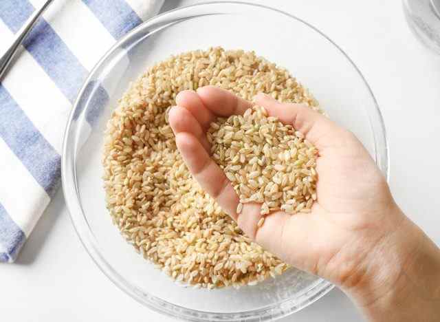 Braunen Reis in der Hand über einer Glasschüssel Reis halten