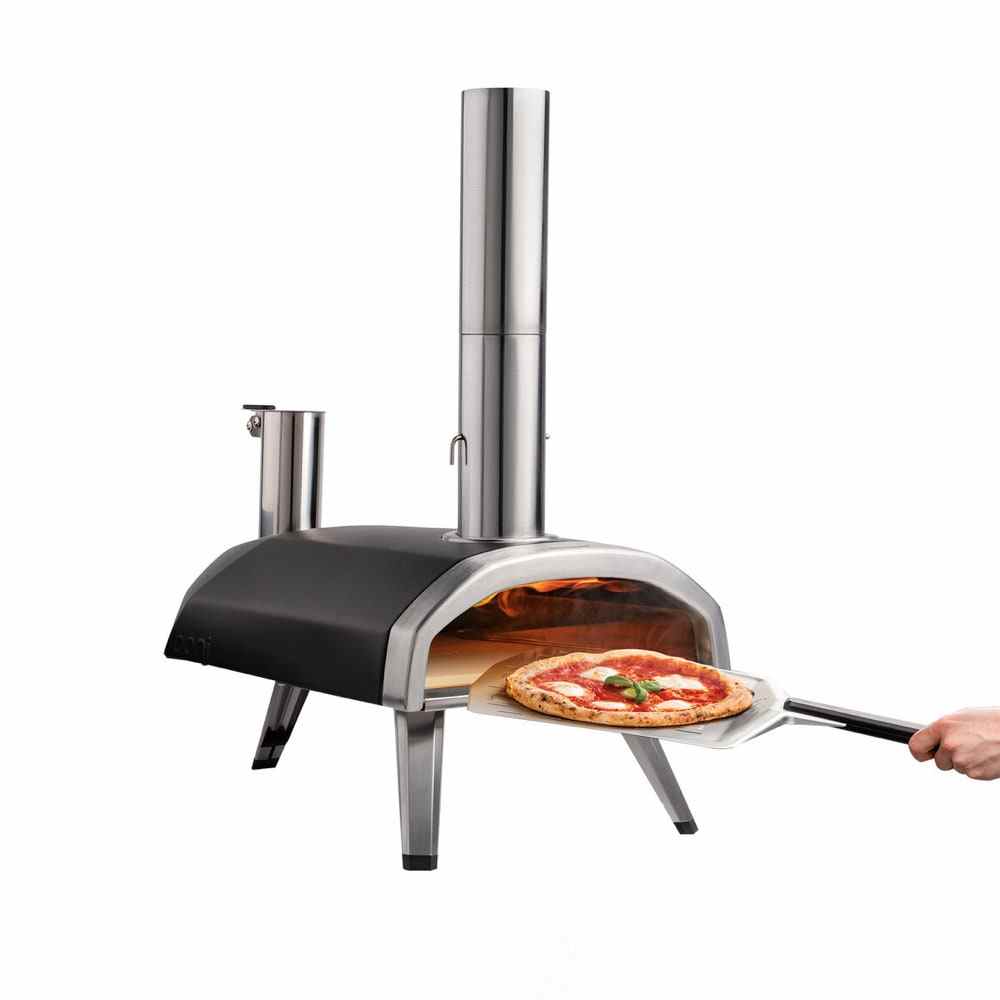Hand, die Pizza auf Metallpaddel in einem schwarzen und silbernen Sur La Table Ooni Fyra 12 Holzpellet-Pizzaofen auf weißem Hintergrund platziert