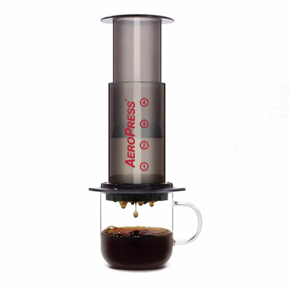 Aeropress Kaffee- und Espressomaschine auf einem durchsichtigen Becher, gefüllt mit Kaffee auf weißem Hintergrund