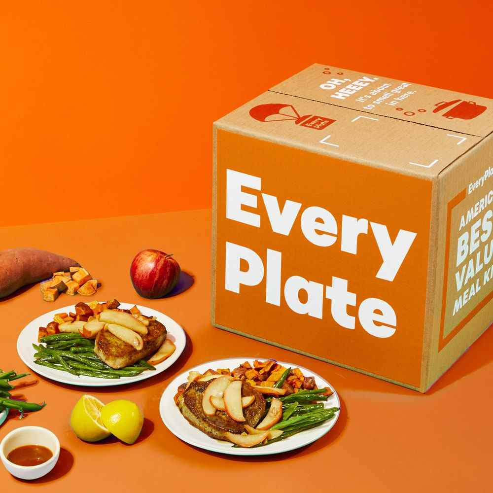 EveryPlate gekochte Speisen auf weißen Tellern und Verpackungen auf orangefarbenem Hintergrund