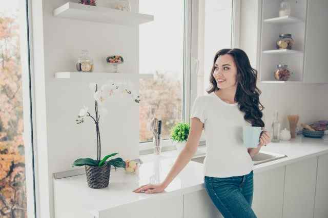glückliche Frau in sauberem Zuhause genießt Kaffee in heller Küche
