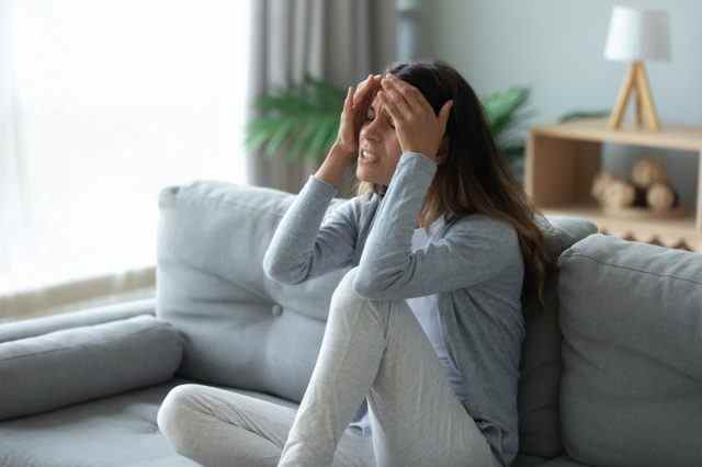 Gestresste unglückliche Frau, die die Stirn berührt und unter starken Kopfschmerzen oder chronischer Migräne leidet