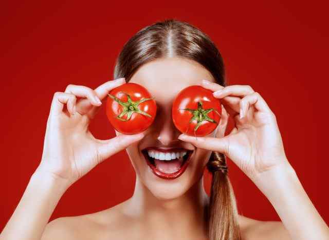 Frau, die Tomaten über ihre Augen hält und lächelt