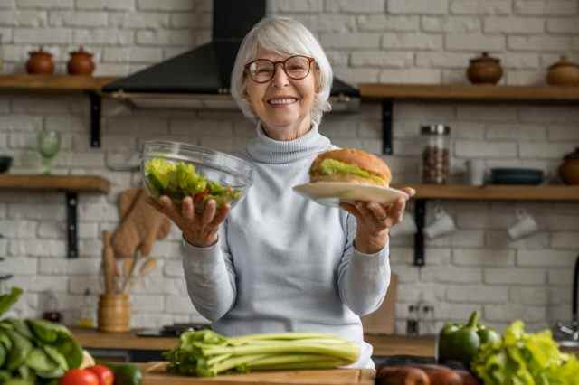 Ältere Frau, die die Wahl zwischen gesundem und ungesundem Essen trifft